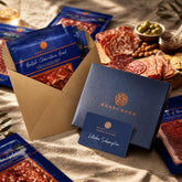Bray Cured letterbox charcuterie subscription gift card in a blue gift box, with packs of British charcuterie in a kraft envelope beside a charcuterie platter